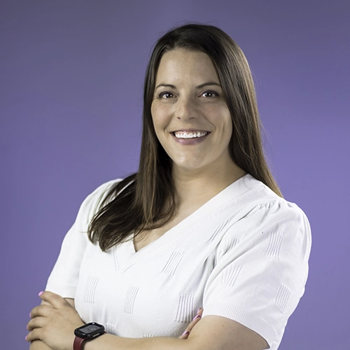 Portrait of a smiling Jeanine Amaro with crossed arms against a purple background.